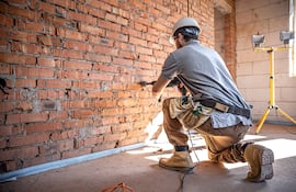 Un operario de mantenimiento en una obra de construcción está perforando una pared con una perforadora.