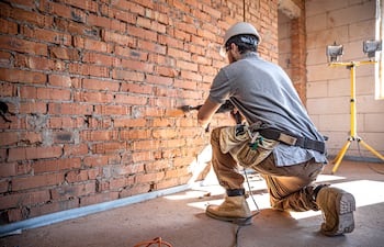 Un operario de mantenimiento en una obra de construcción está perforando una pared con una perforadora.