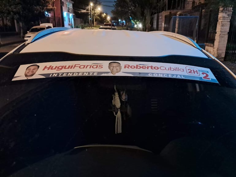 Vehículo con sticker de campaña electoral de Roberto Cubilla y Hugui Farías, en entorno urbano nocturno.