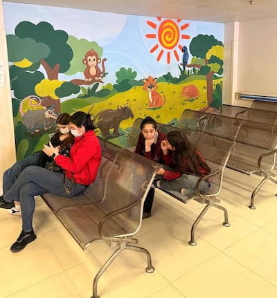 Cuatro personas con mascarillas en banco metálico, conversando. Mural colorido de animales de fondo.