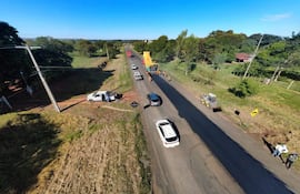 Grupo de trabajadores en ropa amarilla observan la obra en la ruta PY08, con vehículos en movimiento y un paisaje rural de fondo.