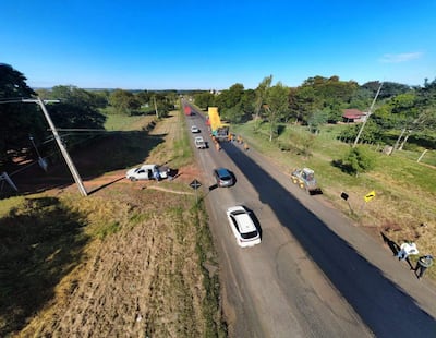 Grupo de trabajadores en ropa amarilla observan la obra en la ruta PY08, con vehículos en movimiento y un paisaje rural de fondo.