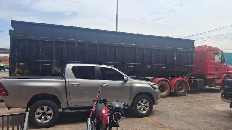 Camioneta plateada y camión rojo estacionados en un área de carga, sin personas visibles en el entorno urbano.