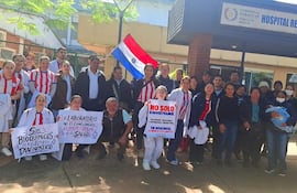 Grupo de bioquímicos con batas y camisetas rojas sosteniendo pancartas sobre la importancia de su labor en la salud.