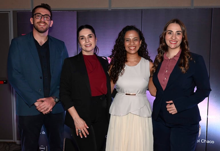 Grupo de cuatro personas sonrientes, dos en blusa roja y vestido blanco claro, en un ambiente formal con decoración sobria.