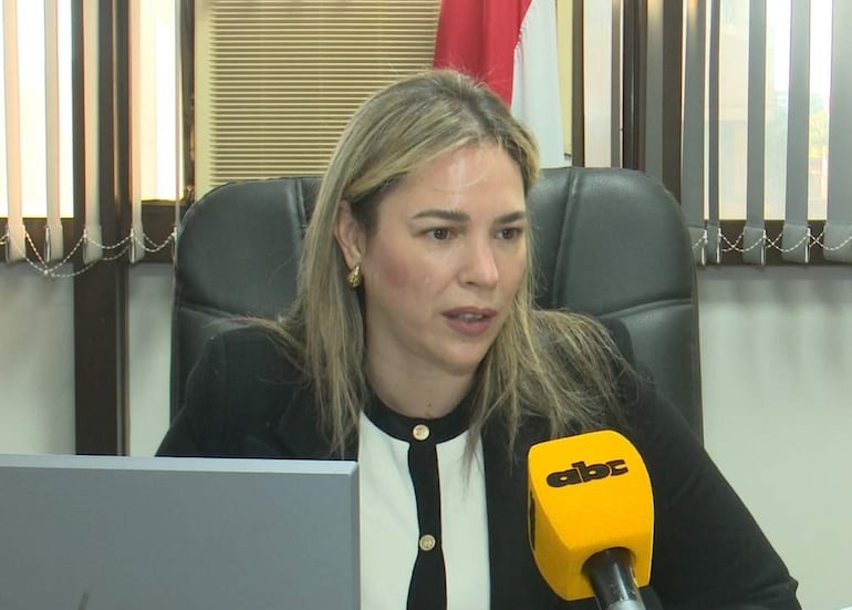 Cecilia Rodríguez con blusa blanca y negra, sentada en un despacho con micrófono amarillo y un monitor en su escritorio.