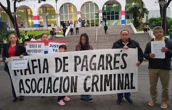Grupo de manifestantes, incluyendo una mujer con pancarta grande sobre mafia de pagarés, frente al Palacio de Justicia.