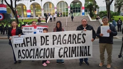 Grupo de manifestantes, incluyendo una mujer con pancarta grande sobre mafia de pagarés, frente al Palacio de Justicia.