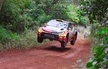 Toyota en salto durante rally, con vegetación densa de fondo y tierra húmeda bajo las ruedas.