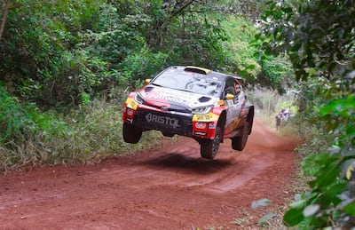 Toyota en salto durante rally, con vegetación densa de fondo y tierra húmeda bajo las ruedas.