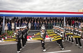 Grupo de militares en uniforme desfilan enérgicamente, con un estrado decorado en rojo, blanco y azul al fondo.