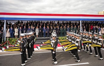Grupo de militares en uniforme desfilan enérgicamente, con un estrado decorado en rojo, blanco y azul al fondo.