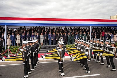 Grupo de militares en uniforme desfilan enérgicamente, con un estrado decorado en rojo, blanco y azul al fondo.