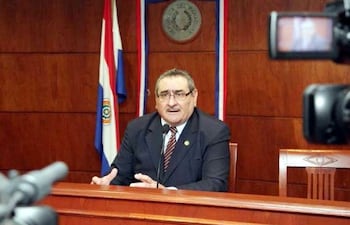 Antonio Fretes en traje oscuro enfatiza un punto mientras gesticula y es grabado por cámaras en un entorno oficial.