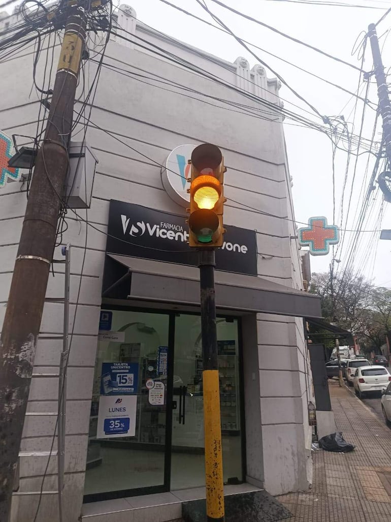 Fachada de la farmacia Vicente B. Z. con semáforo amarillo y vehículos estacionados en un día nublado.