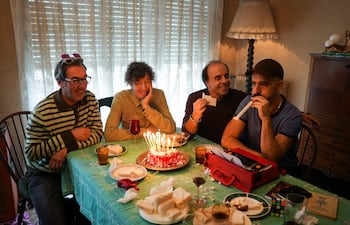 Cuatro personas sonrientes en suéteres, con un pastel en el centro de la mesa, disfrutando de un momento festivo.