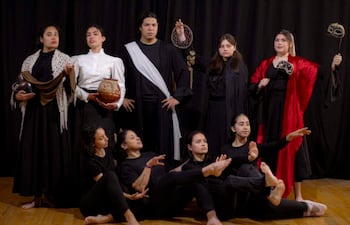 Grupo de ocho artistas en trajes dramáticos negros y acentos rojos, en dinámicas posturas de danza sobre un telón negro.
