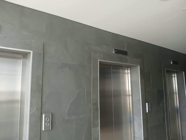 Tres puertas de ascensores apagados con botones al costado, en un ambiente de diseño moderno y minimalista.