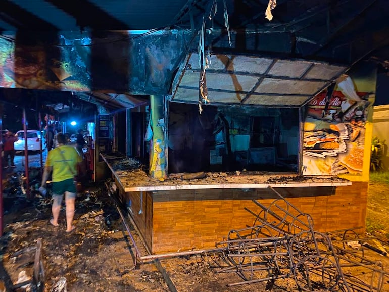 Local gastronómico devastado por el fuego, con estructuras caídas y vehículos estacionados en la calle, sin personas visibles.