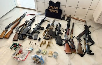 Vista de armas y municiones esparcidas en el suelo, con chaleco de Policía Federal visible en el entorno interior.