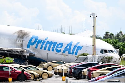 En primer plano se observa un estacionamiento repleto de Tesla Cybercabs, mientras el morro de un avión de carga de Prime Air reposa en el suelo tras haberse salido de la pista y chocado contra varios automóviles el día anterior en el Aeropuerto Internacional de Miami, Florida, el 7 de septiembre de 2026. Al menos cinco personas perdieron la vida cuando un avión de carga de Amazon se salió de la pista tras aterrizar el 6 de septiembre en el Aeropuerto Internacional de Miami, chocó contra vehículos y se incendió, según informaron las autoridades.