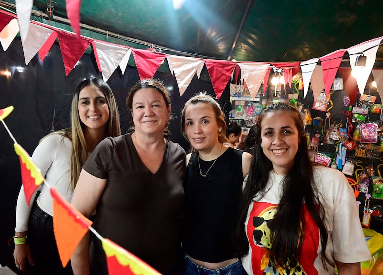 Cuatro mujeres sonrientes, una con camiseta marrón, otra con negro y una más con camiseta blanca, rodeadas de decoraciones festivas.