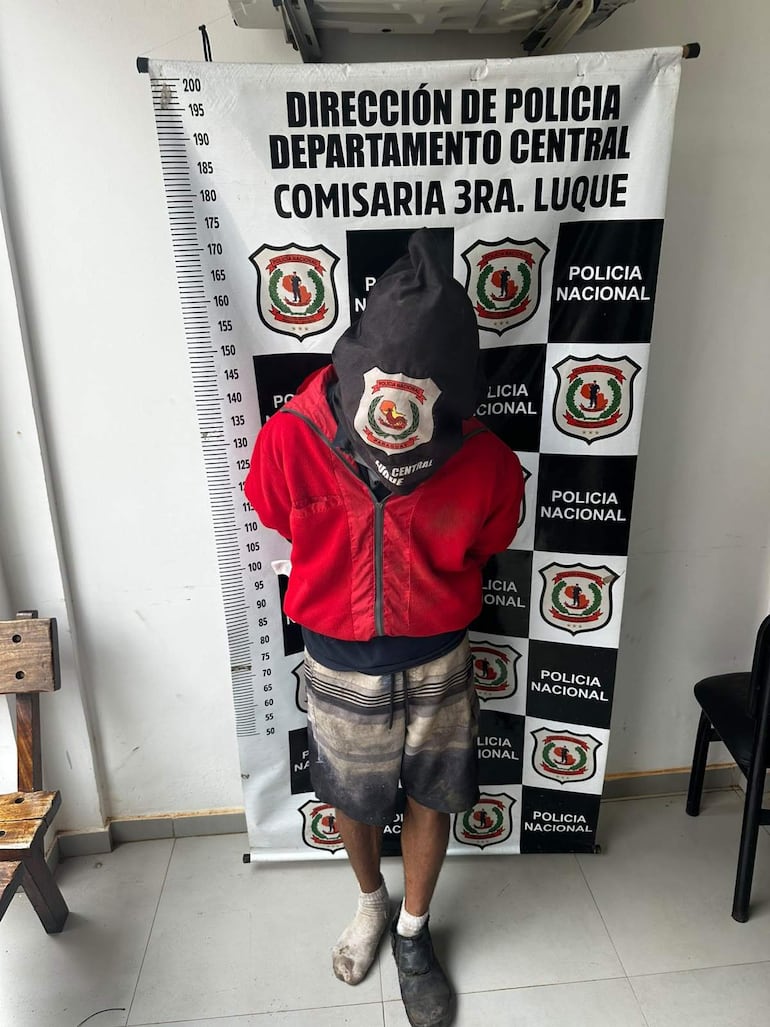 Hombre detenido con saco negro en la cabeza, chaqueta roja y pantalones cortos manchados, en comisaría de Luque.