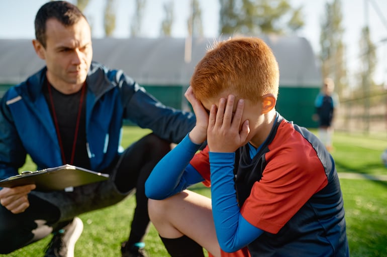 Entrenador consuela a niño triste tras la derrota en un juego deportivo, imagen ilustrativa.