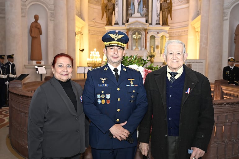 Hombre en uniforme militar con medallas, mujer de cabello rojo en traje oscuro, y hombre mayor con abrigo oscuro, en un ambiente ceremonial.