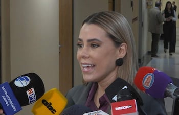 Lizarella Valiente, con cabello lacio y vestimenta formal, habla rodeada de micrófonos en un ambiente institucional.