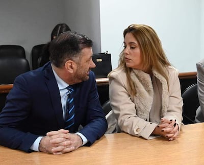 Edgardo Kueider en traje oscuro y corbata a rayas, junto a Iara Guinsel con abrigo claro, en conversación atenta en ambiente interior.