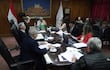 Isaías Ricardo Fretes gesticula mientras habla en reunión, rodeado de hombres en corbata, con banderas de Paraguay al fondo.