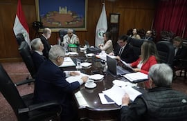 Isaías Ricardo Fretes gesticula mientras habla en reunión, rodeado de hombres en corbata, con banderas de Paraguay al fondo.