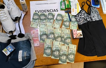 Mesa con productos variados, billetes de guaraní y un frasco de desodorante en un ambiente policial.