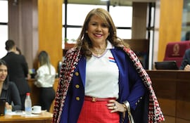 Celeste Amarilla sonriente, vestida con abrigo de cuadros y falda roja, en una reunión con otras personas al fondo.