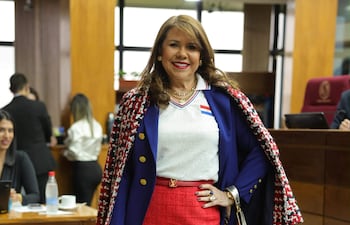 Celeste Amarilla sonriente, vestida con abrigo de cuadros y falda roja, en una reunión con otras personas al fondo.