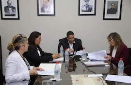 Rocío Vallejo con chaqueta oscura mira documentos mientras José Rodríguez, con chaqueta negra, habla frente a la mesa con botellas de agua.