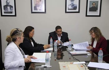 Rocío Vallejo con chaqueta oscura mira documentos mientras José Rodríguez, con chaqueta negra, habla frente a la mesa con botellas de agua.