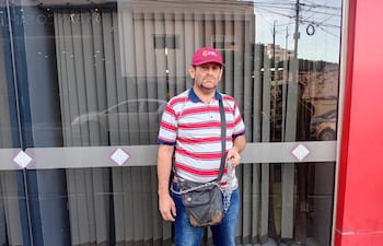 Reinaldo Suárez con camiseta de rayas rojas y blancas y gorro rojo, de pie frente a un edificio, sosteniendo una botella.