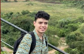 Bruno Rafael Ojeda Alfonsi, joven de cabello rizado, sonríe y levanta el pulgar en un entorno natural con vistas verdes.