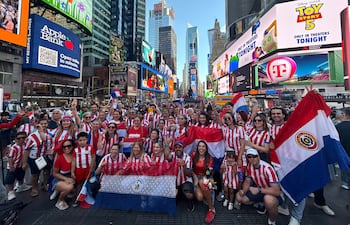 Cincuenta hinchas con camisetas rojas y blancas sonríen y levantan las manos en Times Square, rodeados de banderas paraguayas.