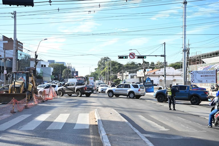 Agente de tránsito en uniforme dirigiendo el tráfico en intersección con vehículos detenidos y camión de construcción amarillo.