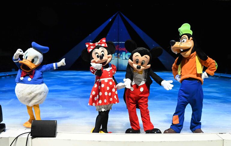 Mickey Mouse, Minnie, Donald y Goofy posan en el escenario de hielo, todos con vestuarios coloridos y posturas amigables.