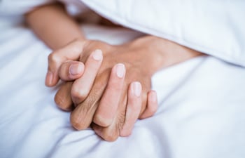 Una pareja se toma de la mano en la cama.