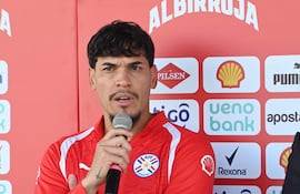 Hombre con camiseta roja de la APF habla al micrófono, mientras se aprecian logos de patrocinadores en el fondo.
