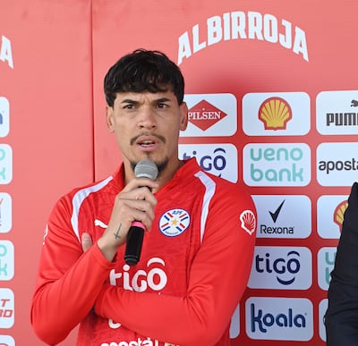 Hombre con camiseta roja de la APF habla al micrófono, mientras se aprecian logos de patrocinadores en el fondo.