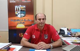 Juan Manuel Santacruz vestido con camiseta roja sentado en un escritorio, con documentos y una computadora en su oficina, luciendo tranquilo.
