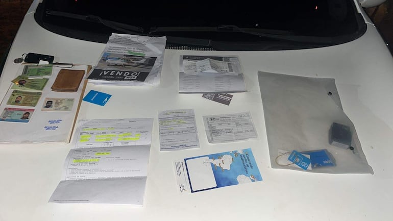 Documentos y objetos sobre un vehículo blanco, incluyendo identificaciones y un folleto de venta de Cessna 210.