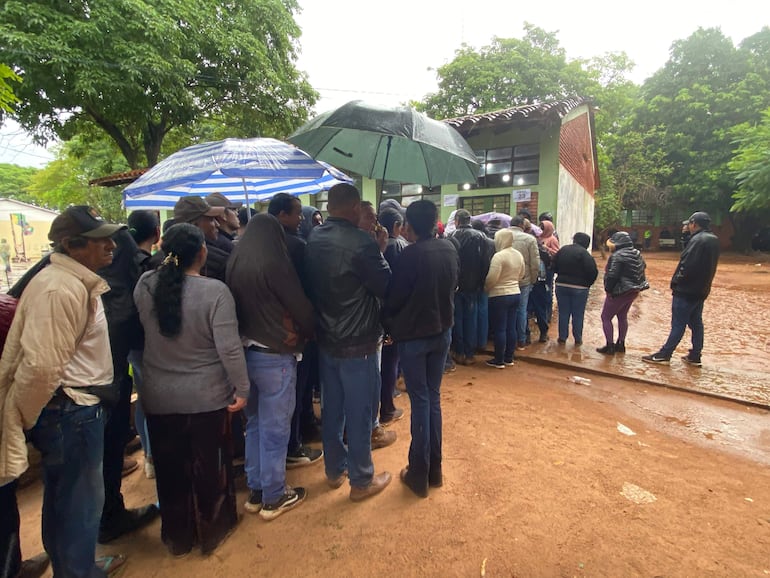 Personas en fila, algunos con paraguas, esperando en un ambiente lluvioso frente a un edificio público en Concepción.