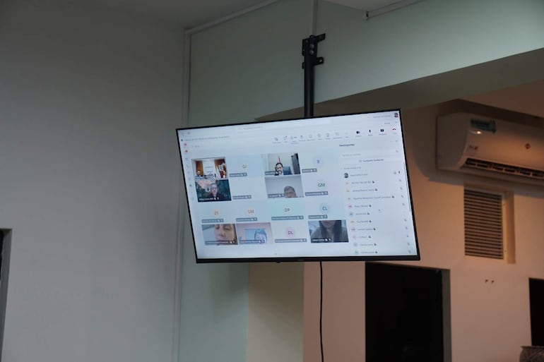 Pantalla de videoconferencia muestra reunión con varios participantes, en un ambiente de oficina sin personas visibles.